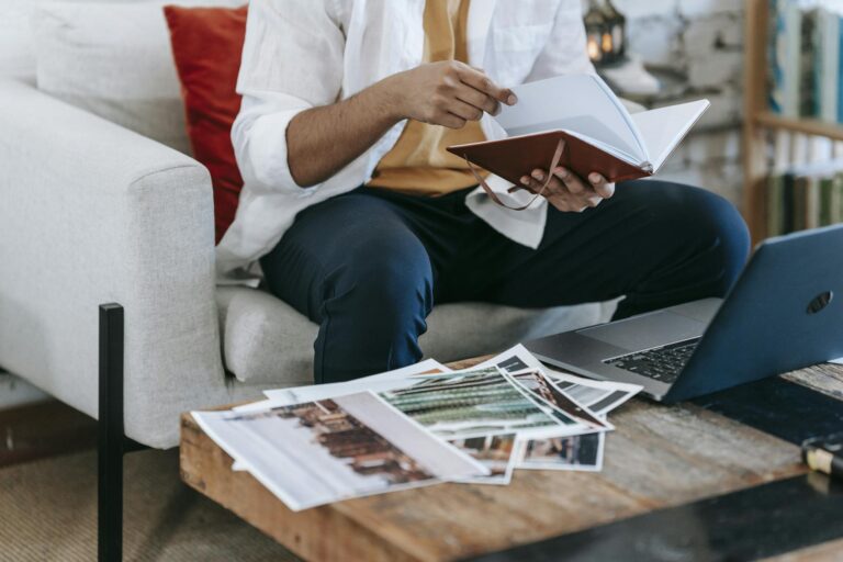 Man reviewing images and notes at a cozy workspace with laptop and notebook.